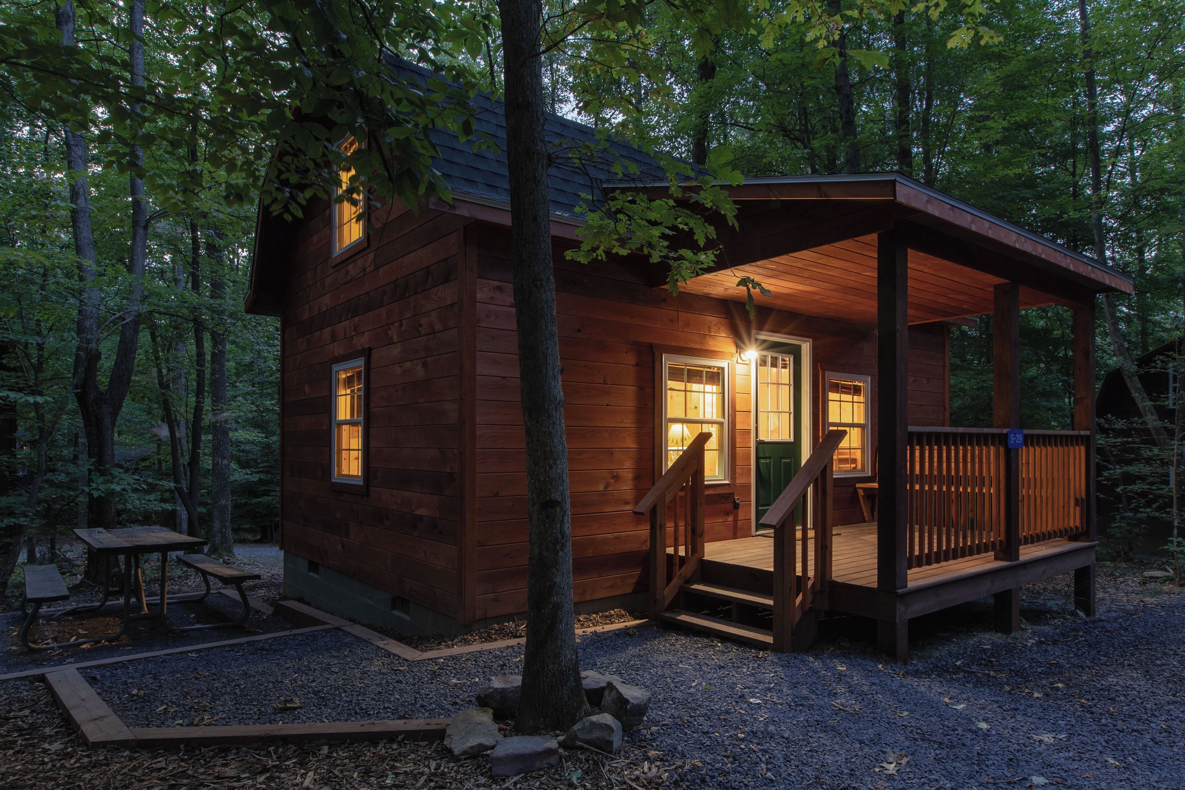 A wooden cabin with a porch, a table, and a bench in a forest setting.