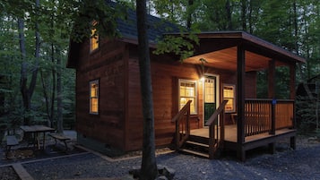 A wooden cabin with a porch, a table, and a bench in a forest setting.
