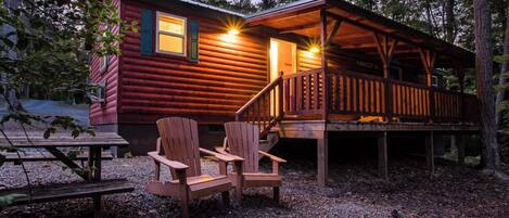 A log cabin with a porch, two Adirondack chairs, and a fire pit.