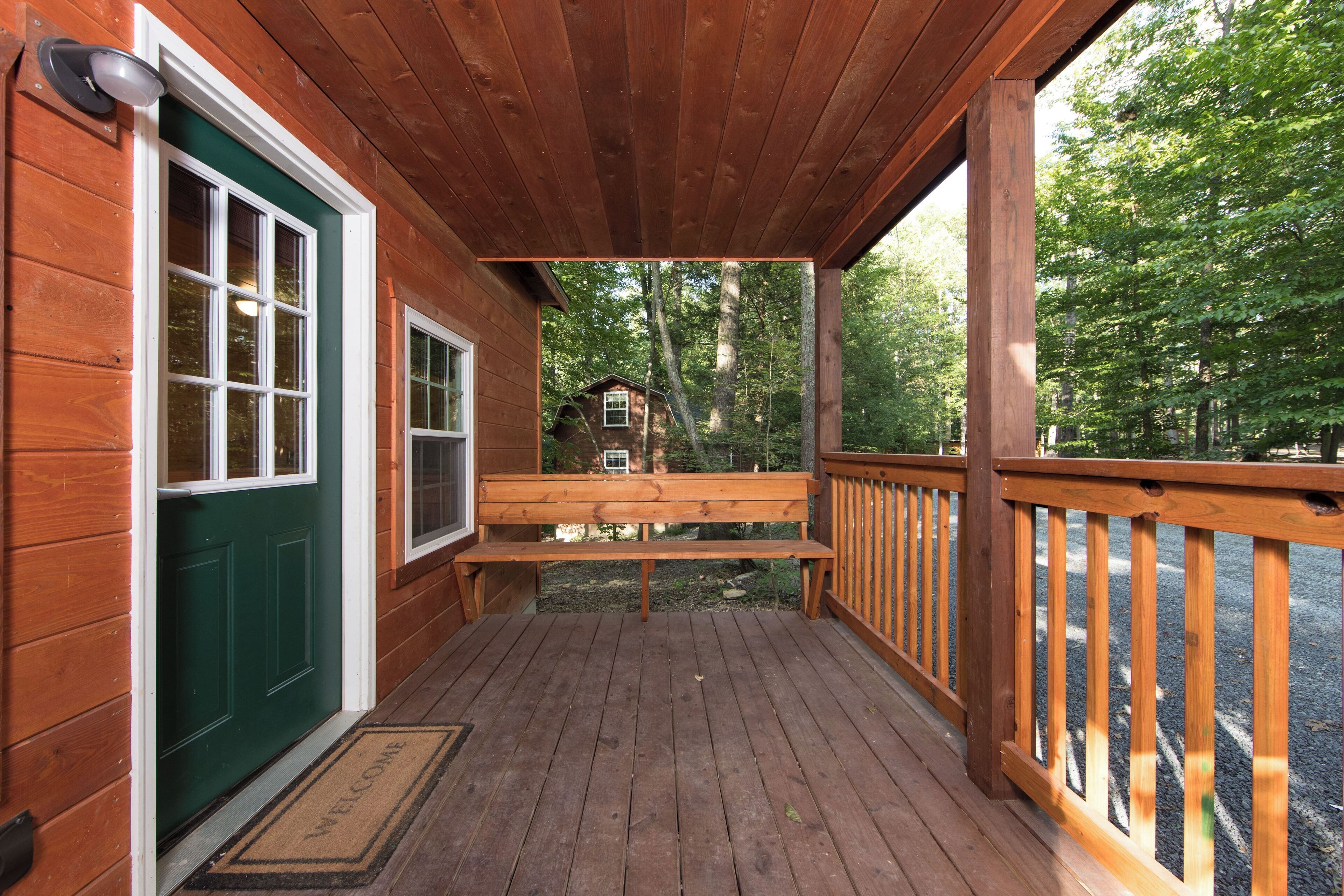 Une terrasse en bois avec un banc, une porte verte et, au loin, la vue sur une cabane.