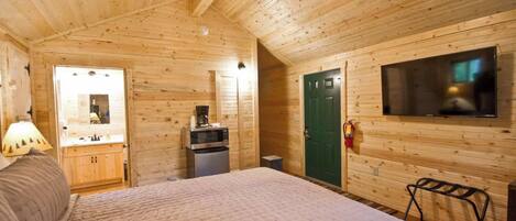 A wooden cabin room with a bed, a TV, a microwave, and a small kitchenette.