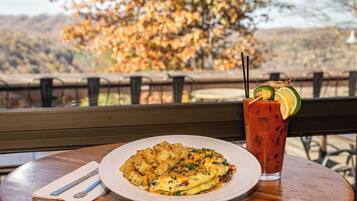 A meal with a plate of food and a drink on a table with a view of autumn trees.