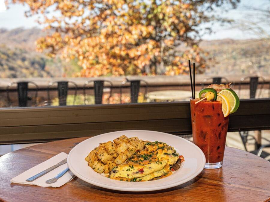 A meal with a plate of food and a drink on a table with a view of autumn trees.