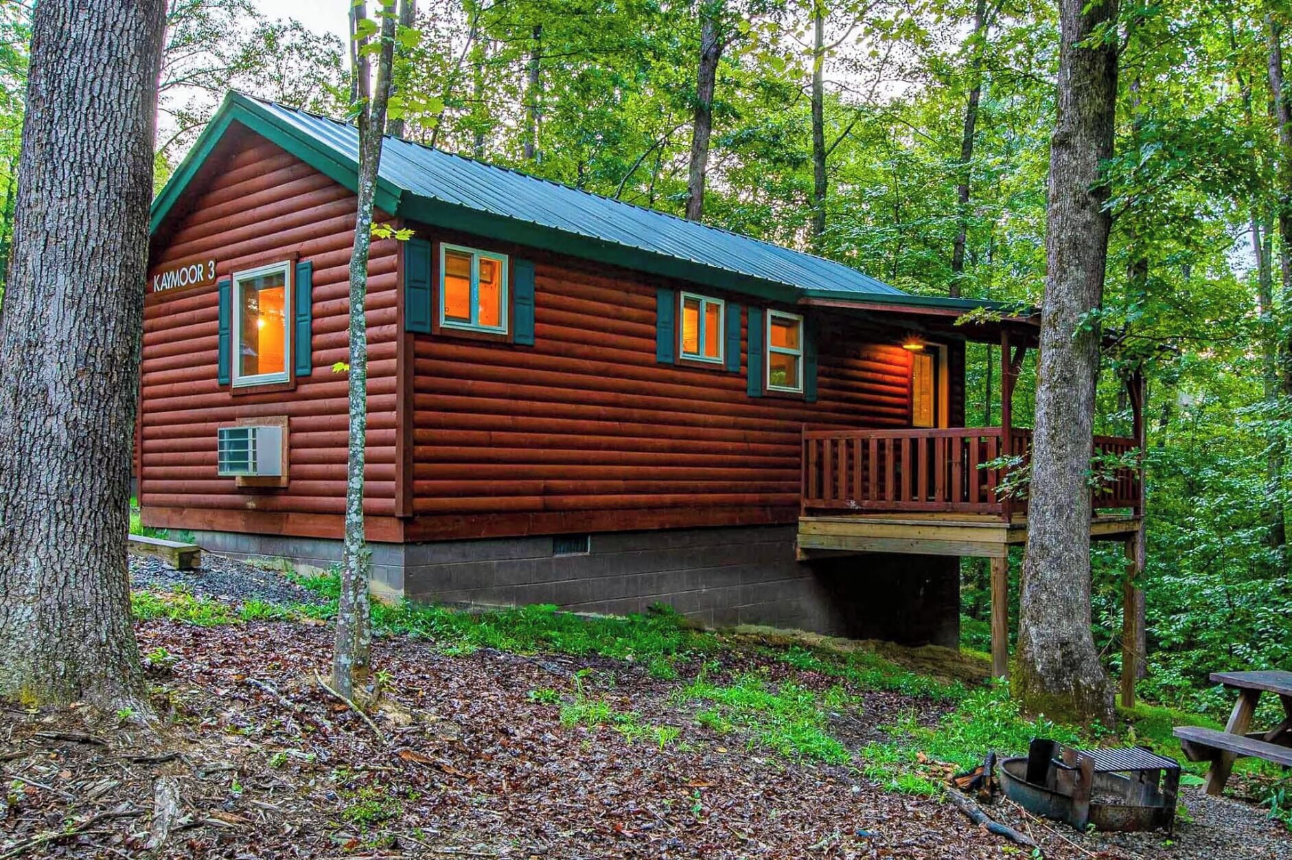 A log cabin with a green roof, a porch, and a deck.