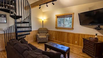 Una sala de estar acogedora con una escalera espiral, un sofá cómodo, piso de madera, una lámpara y un televisor.