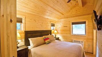 Un dormitorio acogedor de cabaña de madera con una cama, mesitas de noche, una ventana y un ventilador de techo.