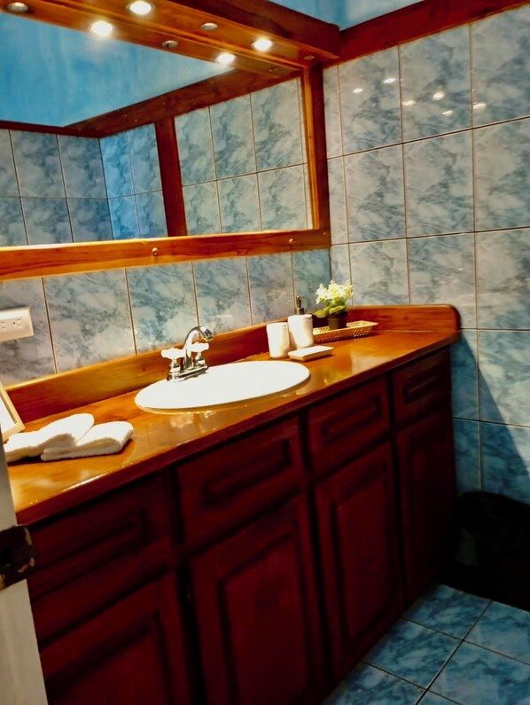 A bathroom with a marble-tiled wall, a wooden vanity with a sink, and a mirror above the vanity.