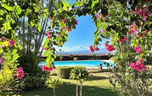 A pool surrounded by lush greenery and pink flowers, with a clear view of a distant mountain range.