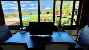 Habitación con vistas a un jardín ajardinado y una piscina, un escritorio con una silla y un florero con flores en el alféizar.