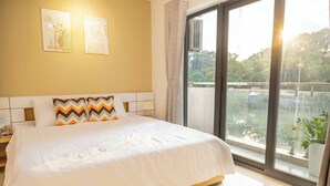 A hotel room with a large bed, a nightstand, a window with a view of the outdoors, and two wall-mounted artworks.
