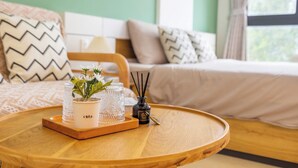 A neatly arranged room with a bed, a bedside table with a tray holding a potted plant, a glass, and a reed diffuser.