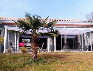Ein Haus mit überdachter Terrasse, einer Palme und einer Garagentür.