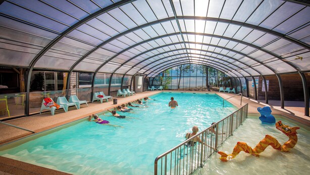 En inomhuspool med klart vatten, omgiven av ett glastak och metallräcken.