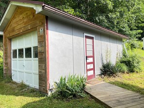 Um pequeno edifício térreo com porta de garagem, porta vermelha e um deck de madeira.