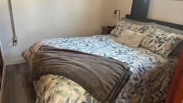 A neatly made bed with floral bedding, a bedside table with a lamp, and a window with curtains.