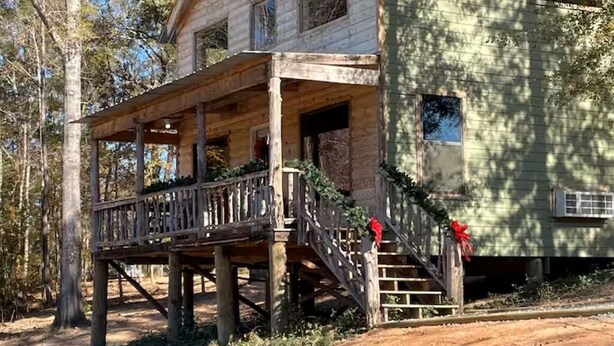 A two-story wooden cabin with a porch and stairs leading to the entrance. - Hidden Oaks Comfy Cabin #7 (Abbeville)