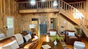 A rustic interior with a wooden staircase, leather sofas, a coffee table, and pendant lighting.