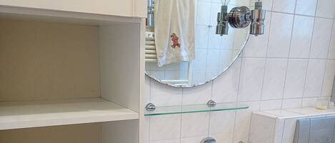 A bathroom with a white sink, a mirror, and a glass shelf.