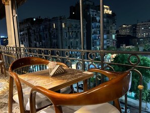 Varanda com mesa e cadeiras, vista para o horizonte urbano à noite.
