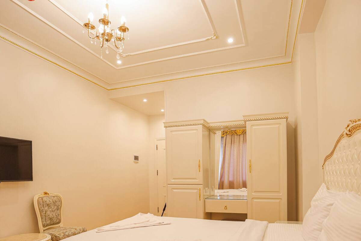 Une chambre avec un grand lit, une chaise, une armoire et un téléviseur fixé au mur.