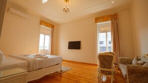 Een slaapkamer met een bed, een stoel, een bank, een televisie en een raam met gordijnen.