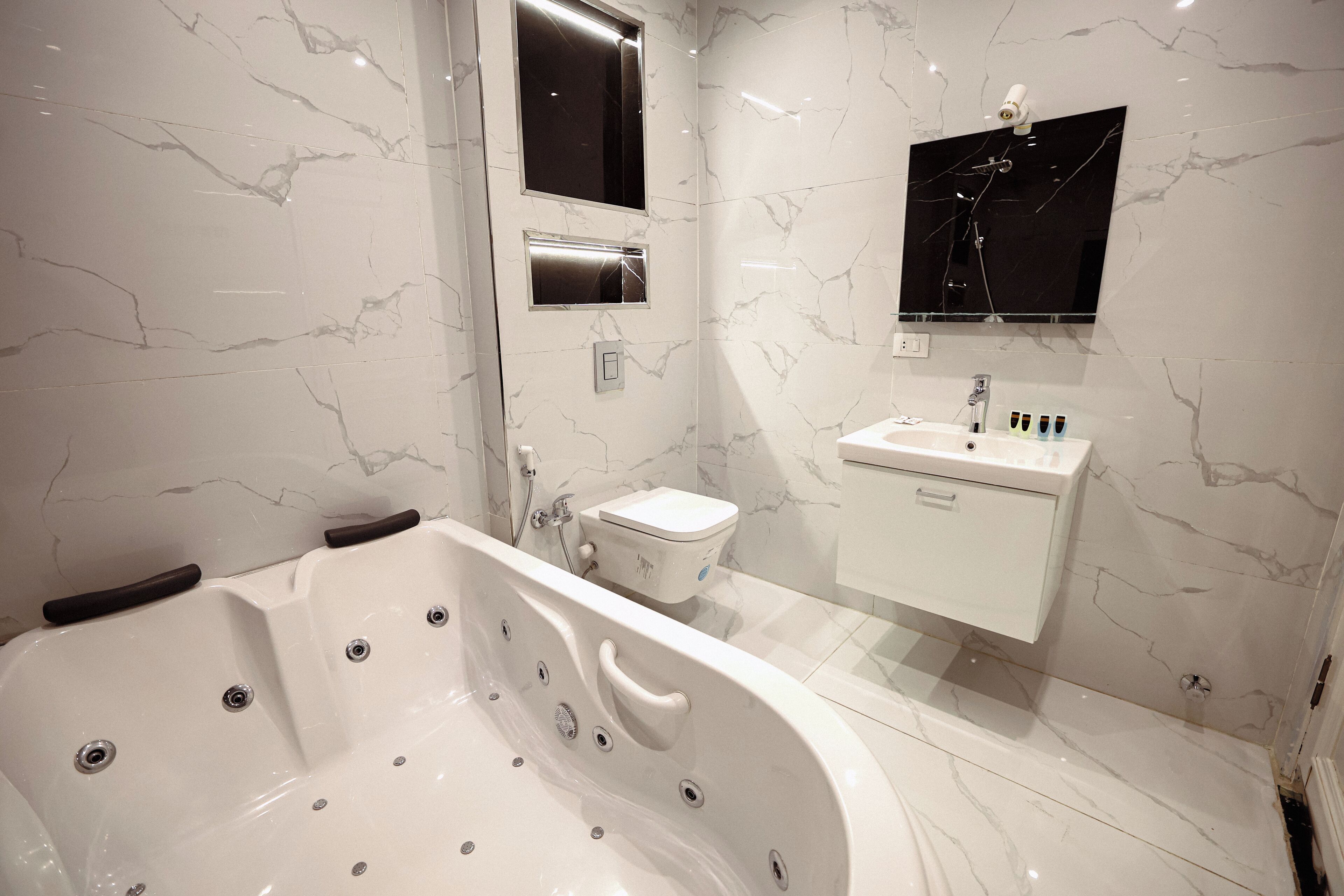 A modern bathroom with a large bathtub, a toilet, and a sink with a mirror above it.