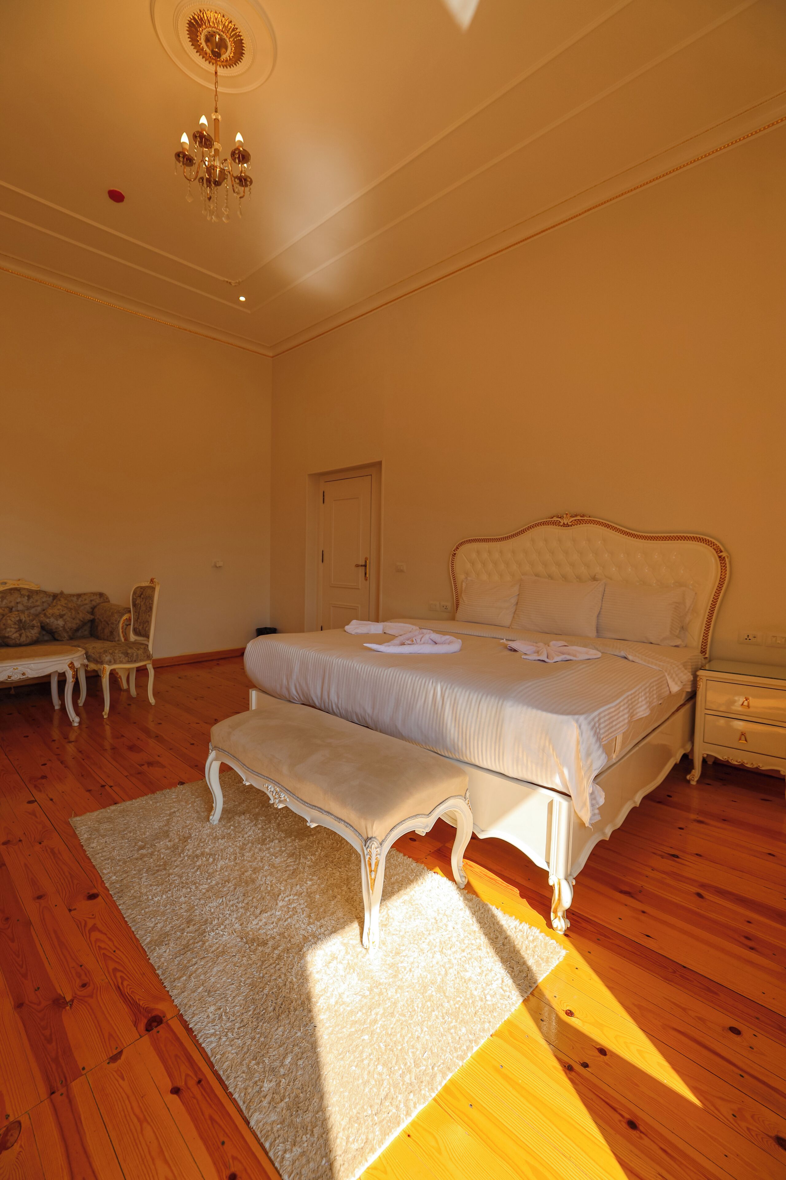 A bedroom with a large bed, a bench, a chair, a nightstand, and a chandelier.