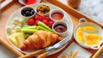 Una bandeja con un croissant, queso, tomates, aceitunas y varias salsas.