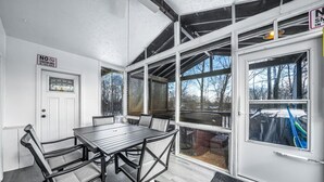 Uma sala de sol com mesa e cadeiras, janelas amplas e um aviso de 'Não Fumar'.