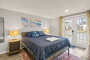 A bedroom with a bed, two bedside tables, a window, and artwork on the wall. - Your Group's Home Base | Downtown | Hot Tub+Games (Watkins Glen)