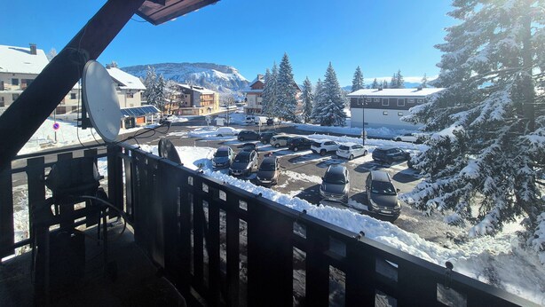 A balcony with a view of a snowy parking lot and buildings, including a hotel with a mountain backdrop.