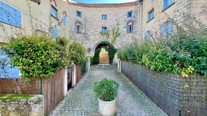 Une ruelle étroite pavée, bordée de bâtiments en pierre dotés de portes en arc de cercle et de volets bleus.