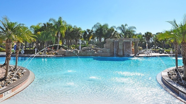 A clear blue pool with a waterfall feature, surrounded by palm trees and rocks.