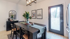 Una cucina moderna con un tavolo da pranzo, sedie, un armadietto nero, una pianta in vaso e quadri appesi al muro.