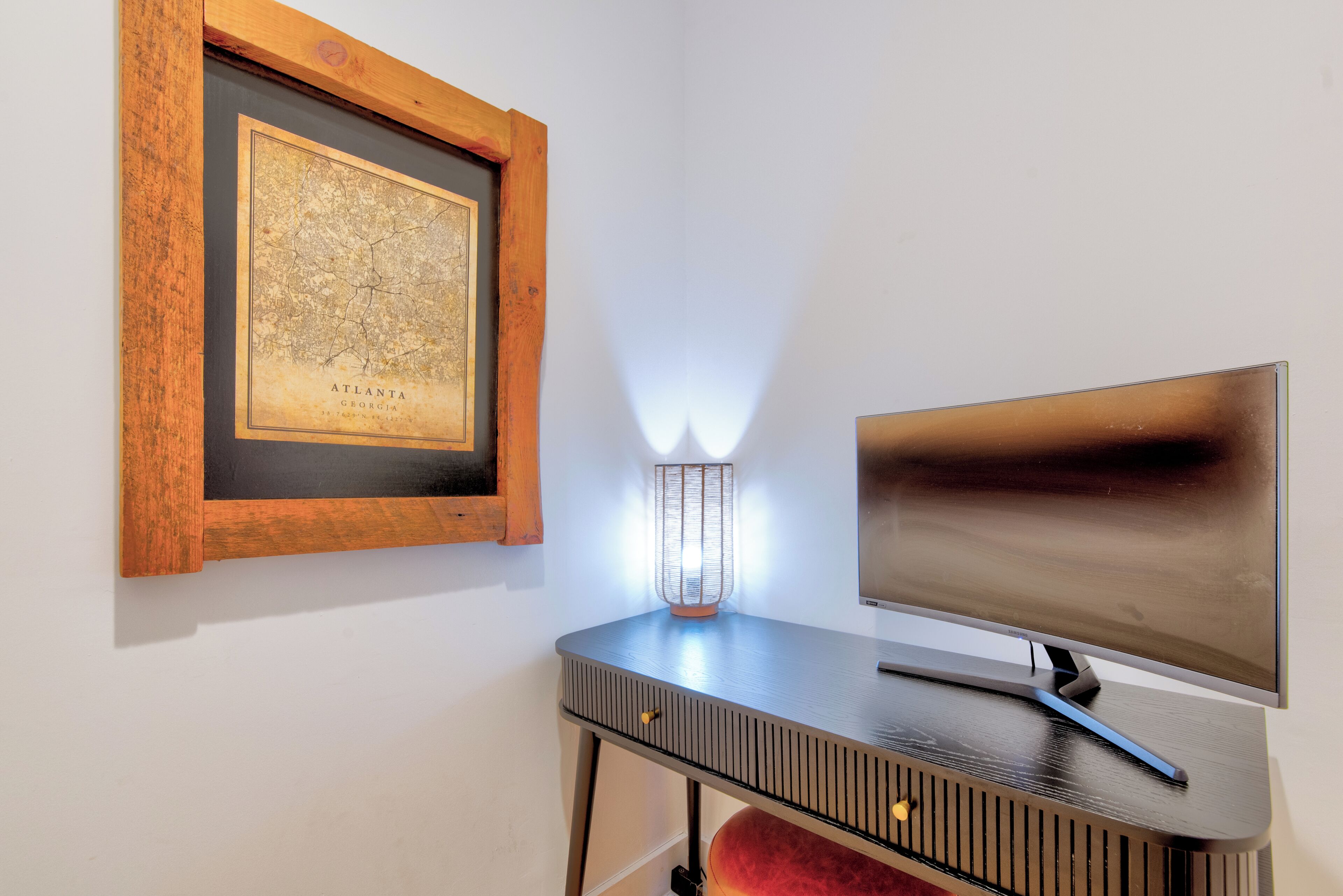 Een ingelijste kaart van Atlanta, Georgia, een modern bureau met een lamp en een flatscreen televisie.