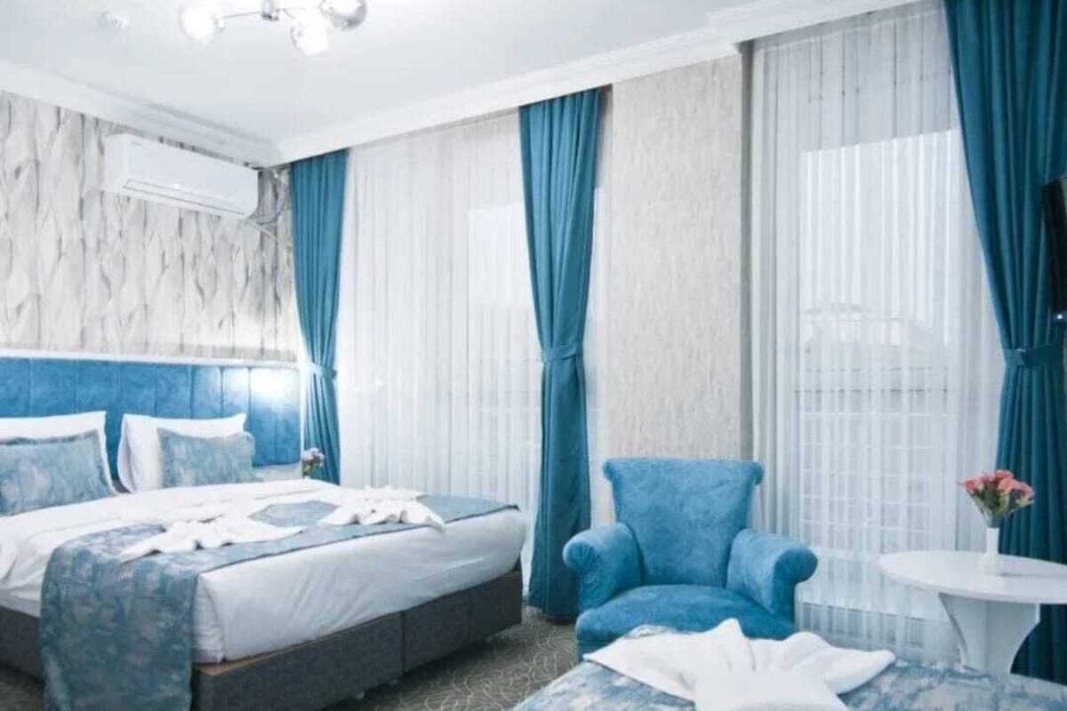 A hotel room with a large bed, a blue armchair, a small round table, and a wall-mounted TV.