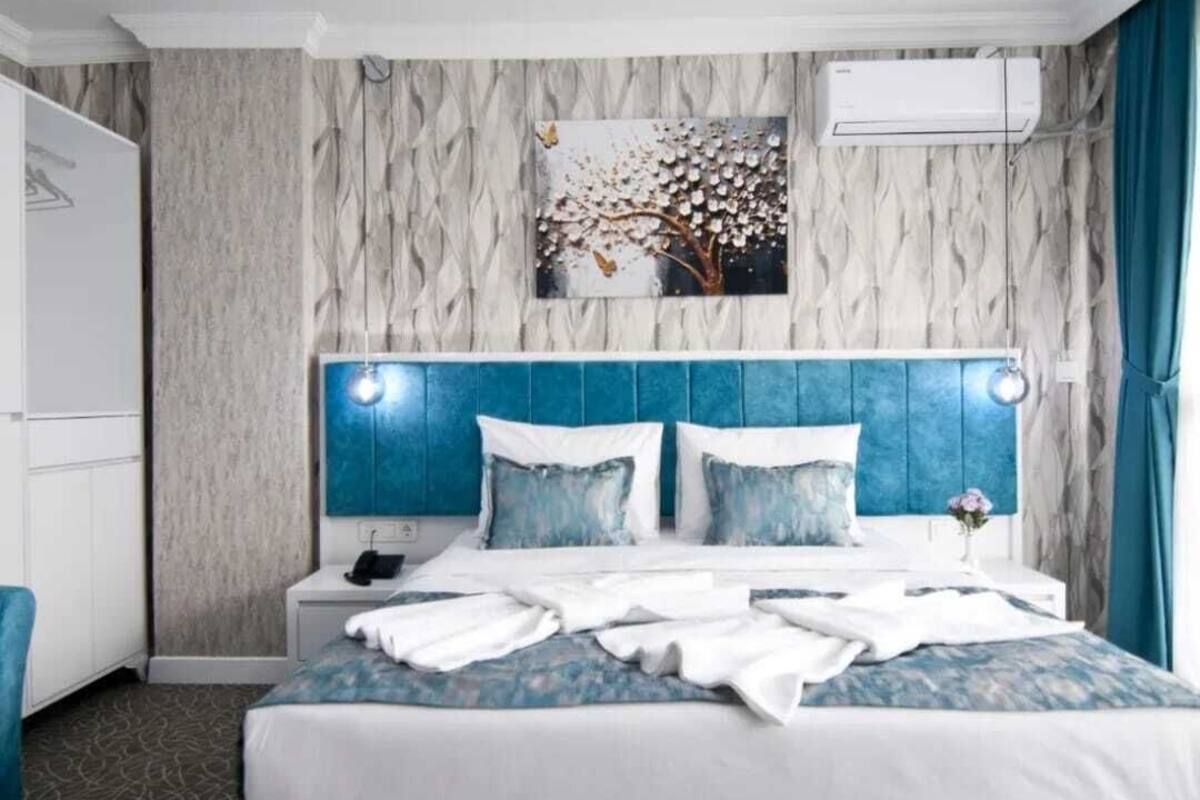 A hotel room with a bed, a nightstand, a wall-mounted air conditioner, and a painting of a tree.