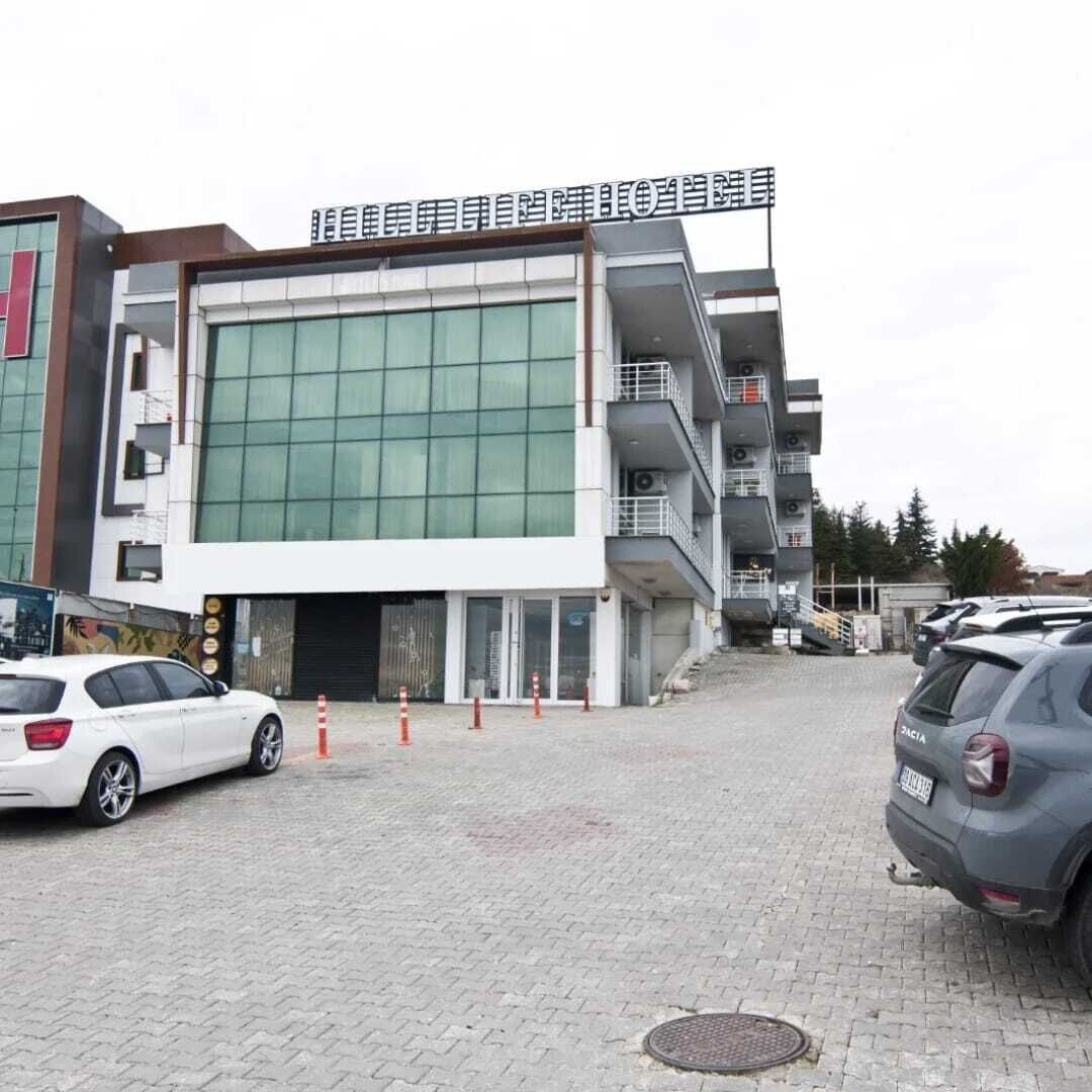 A modern building with a large glass facade, a parking area with cars, and a sign above the entrance.