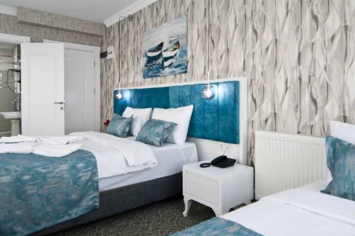 A hotel room with a bed, bedside tables, a nightstand, a painting on the wall, and a patterned wallpaper.