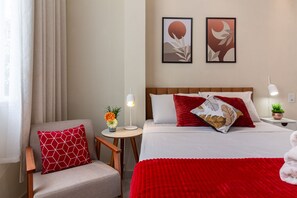 Relax in a stylishly designed room with a neatly made bed, comfortable armchair, and a small table with a lamp and vase of flowers.
