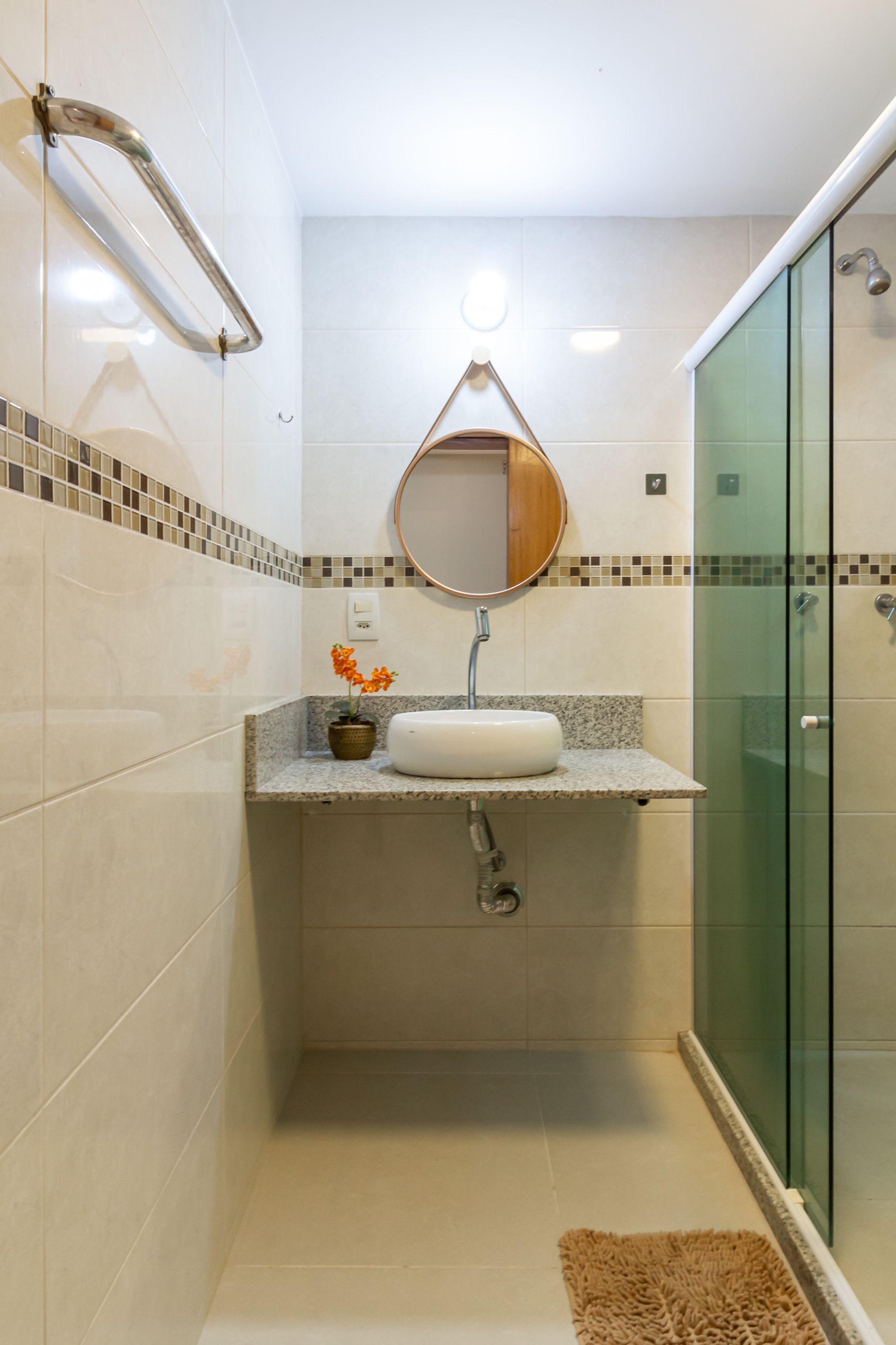 Une salle de bain avec une douche à parois de verre, un lavabo avec un miroir au-dessus et une petite plante en pot posée sur le comptoir.