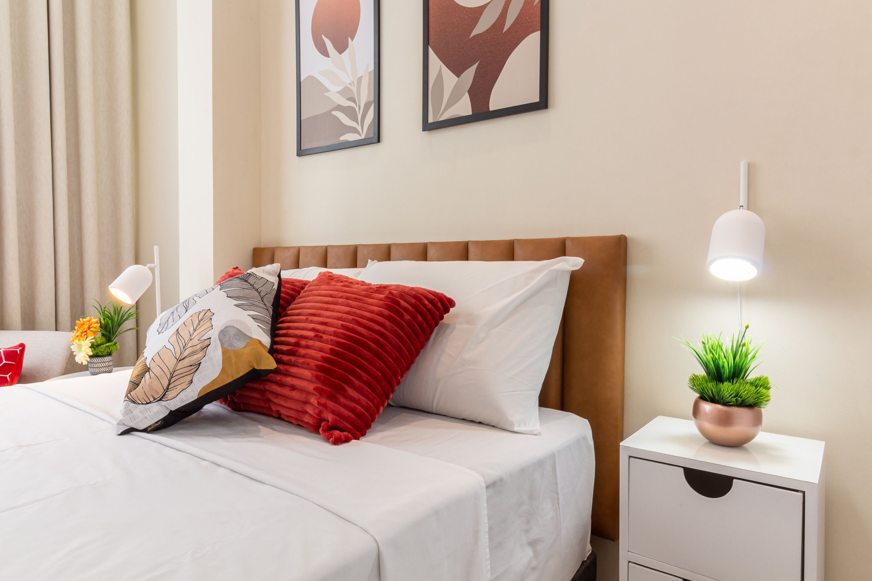 A neatly made bed with white and red bedding, a wooden headboard, and a bedside table with a plant.