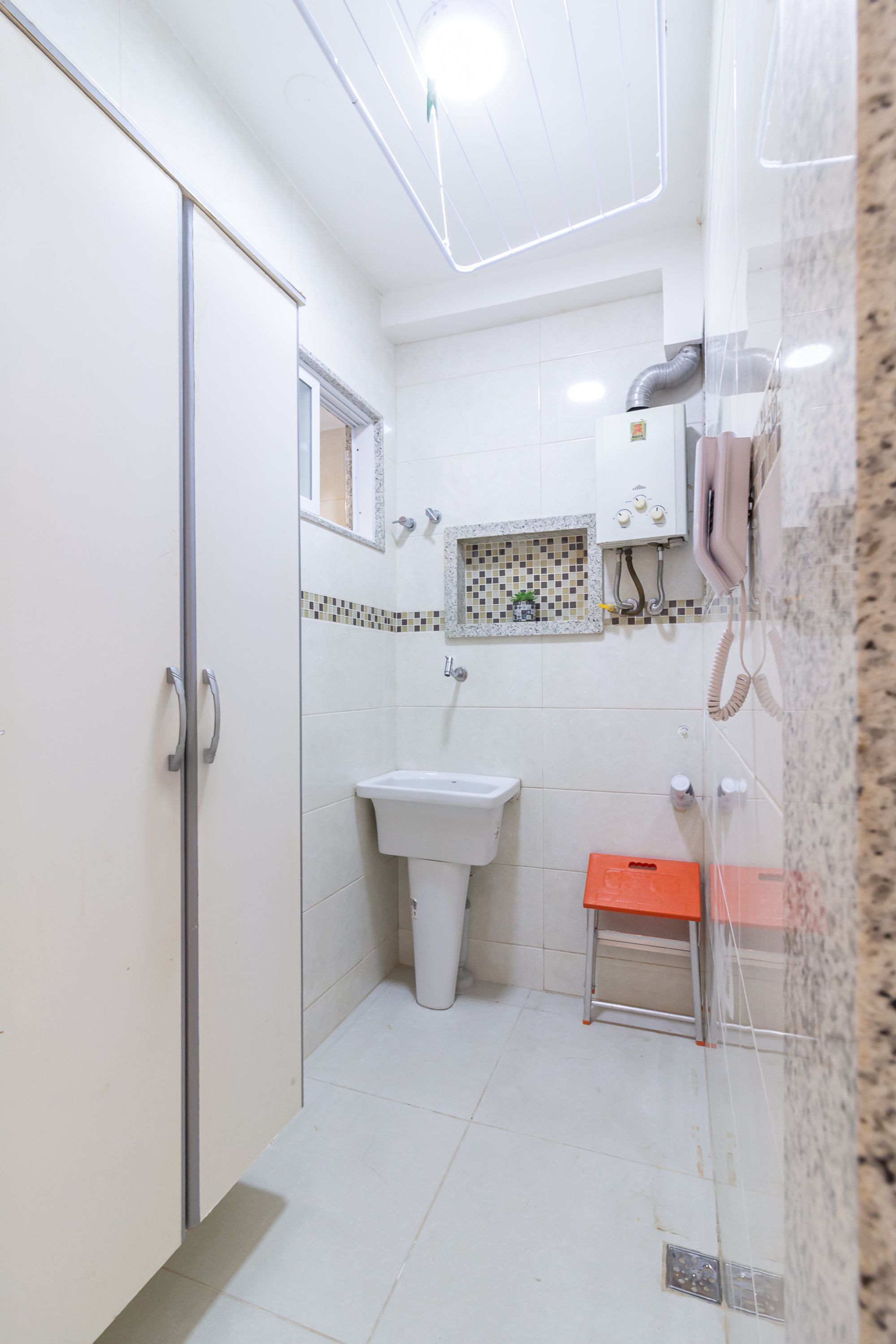 A bathroom with a glass shower enclosure, a white sink, and a small orange stool.
