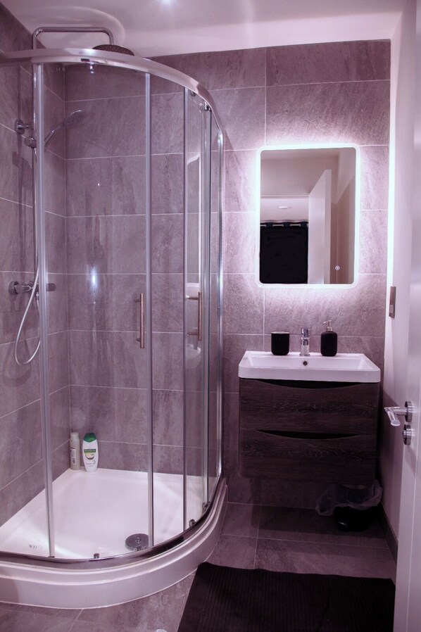 Un baño moderno con ducha de vidrio, tocador con espejo y lavamanos.