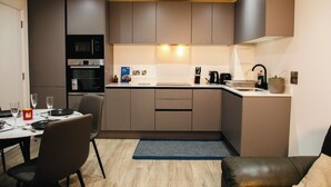 A modern kitchen with a dining area, featuring a built-in oven, a coffee machine, and a sink.
