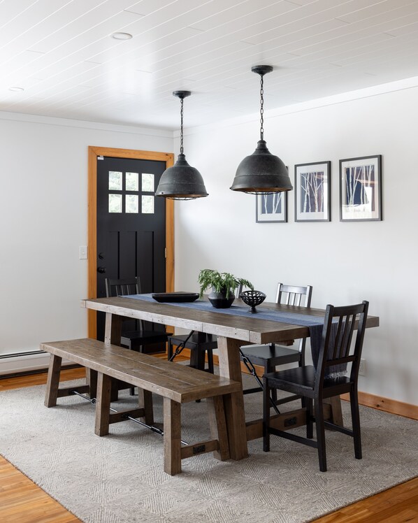 A dining area with a wooden table, benches, and two hanging pendant lights. - Stellar Mountain House:  Luxury - Hot Tub, Views, Near Stowe and Smugglers' (Jeffersonville)