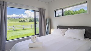 Ein Schlafzimmer mit einem großen Bett, Blick auf ein grünes Feld und Berge, sowie ein Fenster mit Vorhängen.