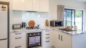 Eine moderne Küche mit weißen Schränken, einem Gasherd, einem Backofen, einer Mikrowelle und einem großen Fenster mit Vorhängen.