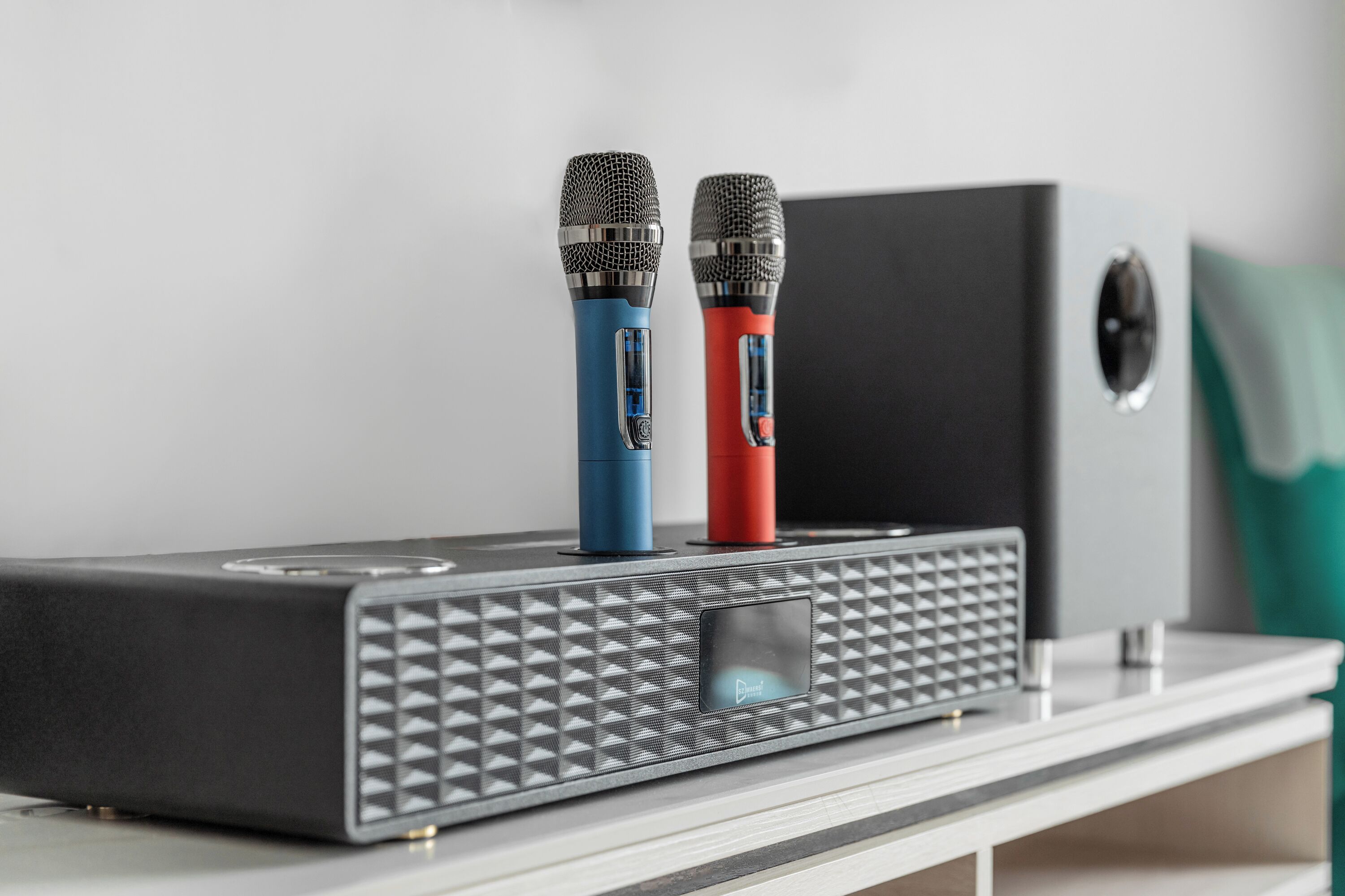 A black speaker with two microphones on top, a small display, and a control panel.