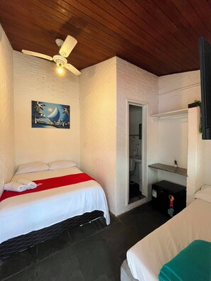 Ein Zimmer mit einem Bett, einem Deckenventilator, einem Gemälde, einem Badezimmer und einem kleinen Regal.